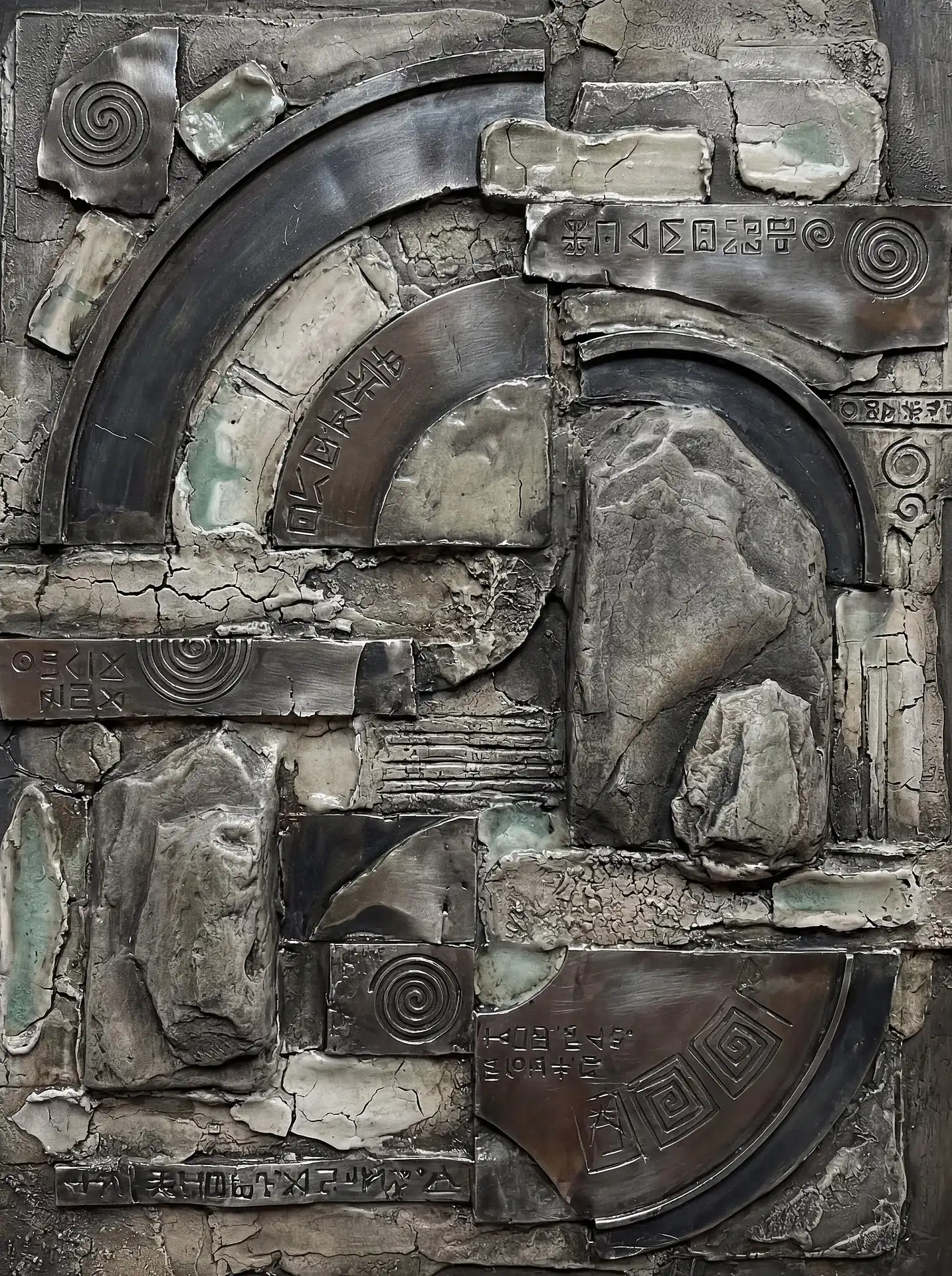 Cool grey lighting illuminates the intricate textures of this wall-mounted relief featuring metallic arcs and engraved runic symbols. This industrial-style sculpture combines geometric metal shapes with organic cracked stone and mystical spirals to create a sense of archaeological discovery. Artwork by Constantine Cheshire