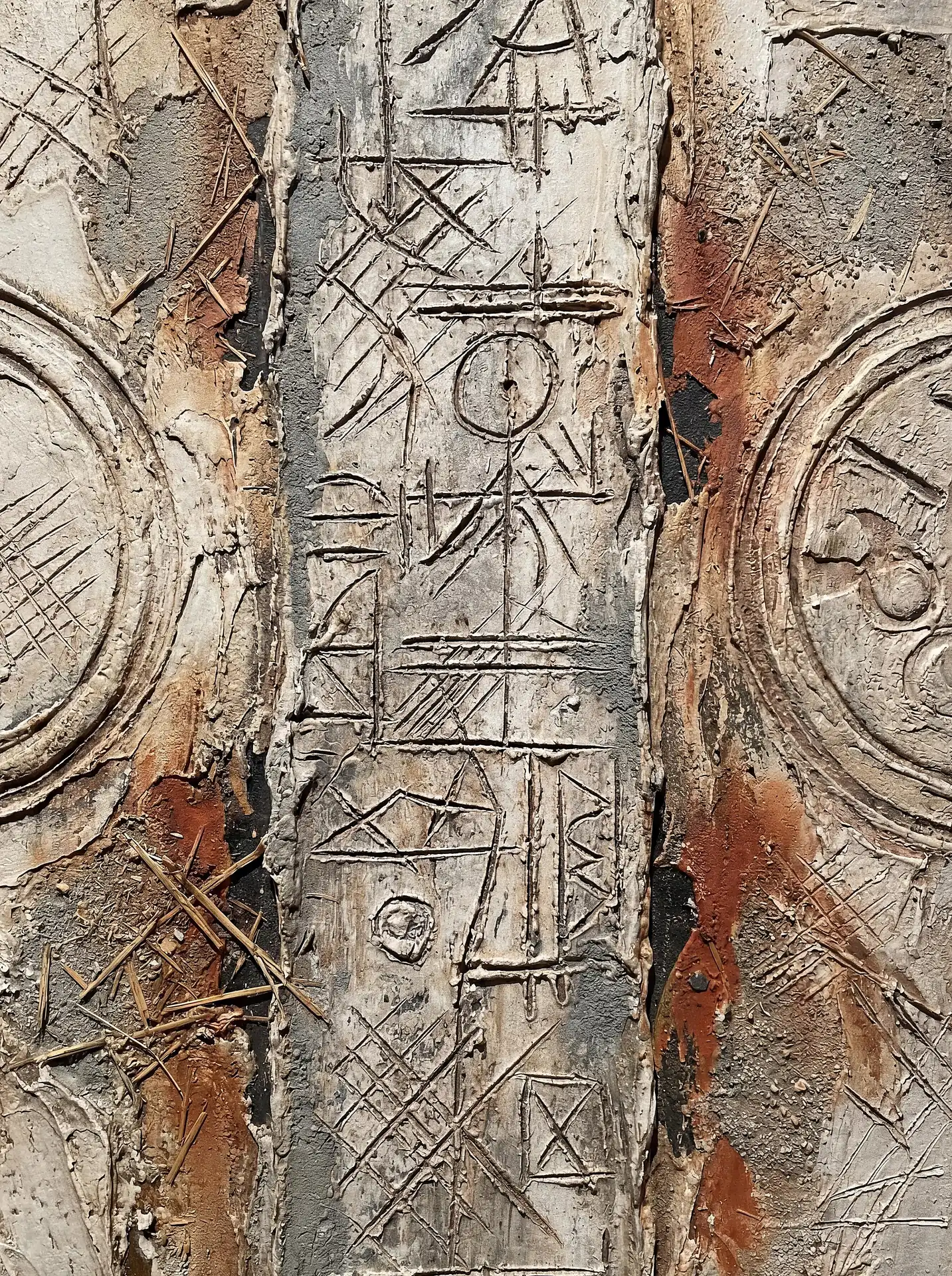 An ancient and mysterious atmosphere emanates from this heavily textured surface featuring hand-carved primitive symbols and embedded organic fibers. Earthy tones of rust and cream highlight the deep grooves and scratched patterns of this mixed media relief. Artwork by Constantine Cheshire