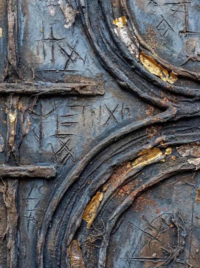 Deep slate blue tones provide a moody backdrop for this textured piece featuring raised organic ridges and etched ancient runes. Flakes of metallic gold leaf catch the light, adding a touch of elegance to the rugged, weathered surface of this mixed media artwork. Artwork by Constantine Cheshire