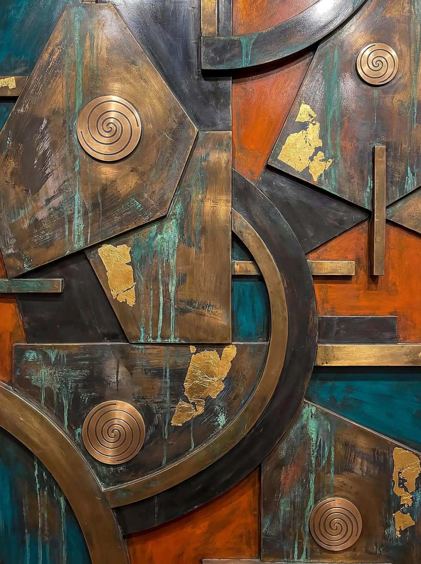 Layering of geometric metal plates creates a complex industrial relief featuring etched copper spirals, gold leaf accents, and natural teal oxidation. This mixed-media sculpture blends warm bronze and orange tones with weathered textures to create a sophisticated, ancient atmosphere. Artwork by Constantine Cheshire