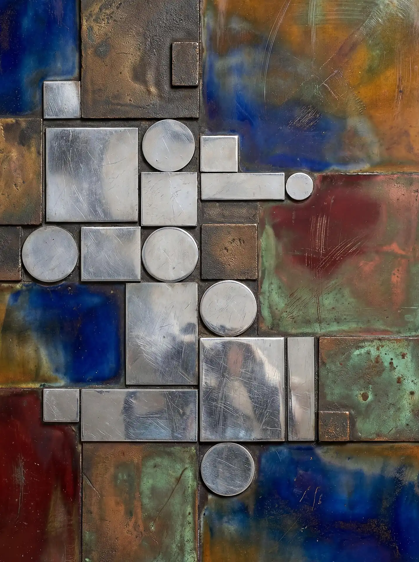 Deep blue and copper-toned patinas cover this abstract metal assemblage of overlapping circles and rectangles. This modern industrial piece features heavily scratched textures and weathered metallic surfaces for a rugged, architectural aesthetic. Artwork by Constantine Cheshire