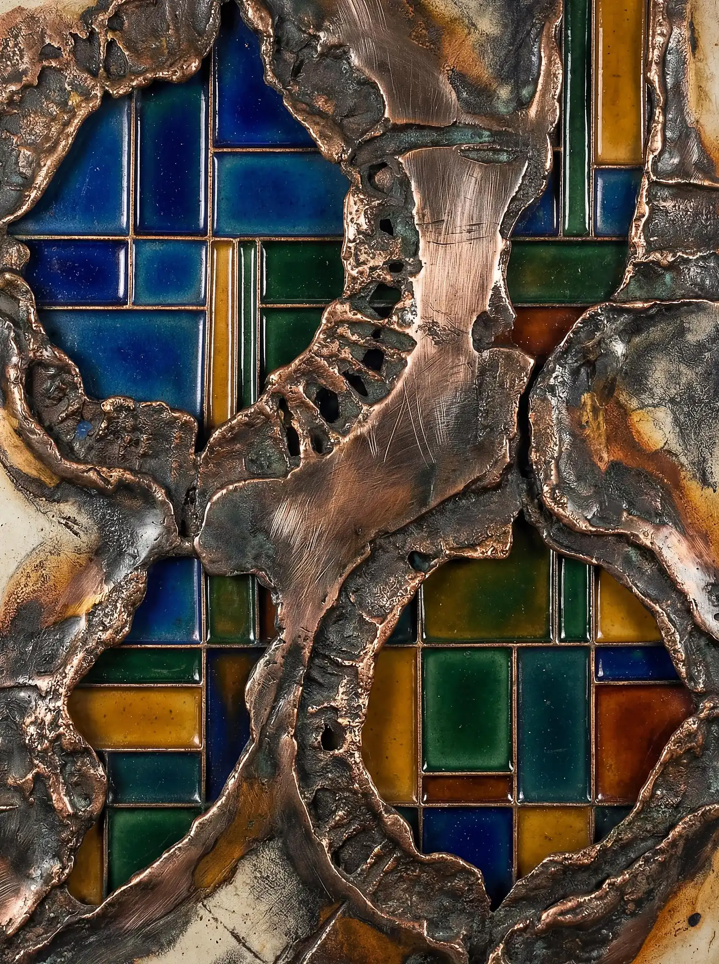 Composition of layered organic metal shapes over a rigid grid of vibrant ceramic tiles creates a striking contrast in this mixed-media piece. The artwork features weathered copper textures against smooth rectangular glass pieces in deep blue, forest green, and mustard yellow. Artwork by Constantine Cheshire
