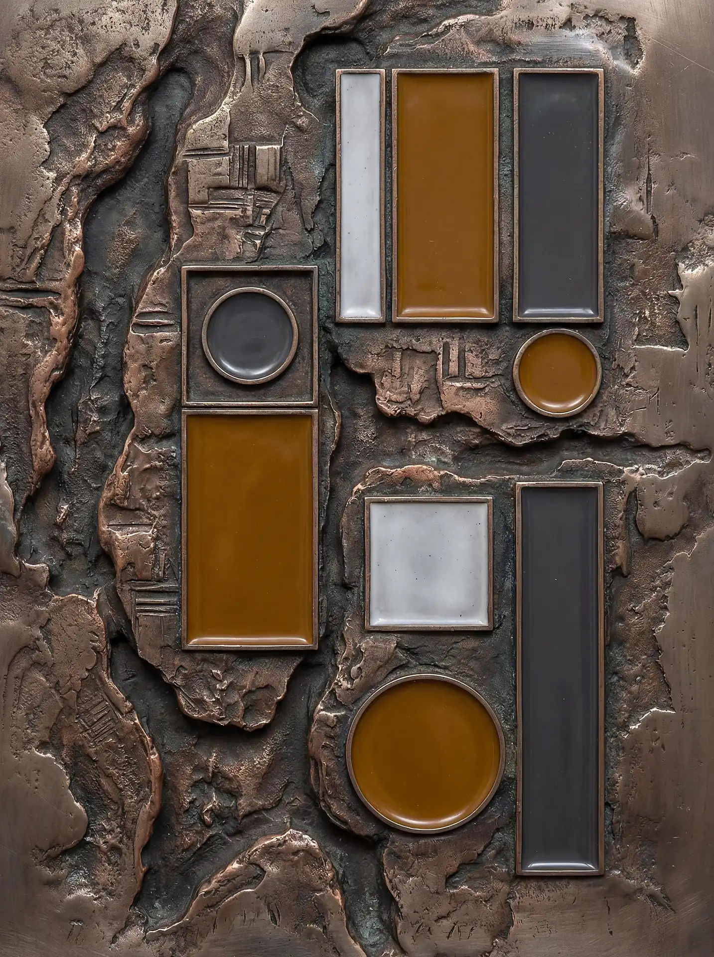 Weathered bronze and smooth enamel textures create a compelling abstract composition of geometric rectangles and circles. This industrial wall relief features a palette of earthy ochre, slate grey, and off-white set against a rugged metallic background. Artwork by Constantine Cheshire