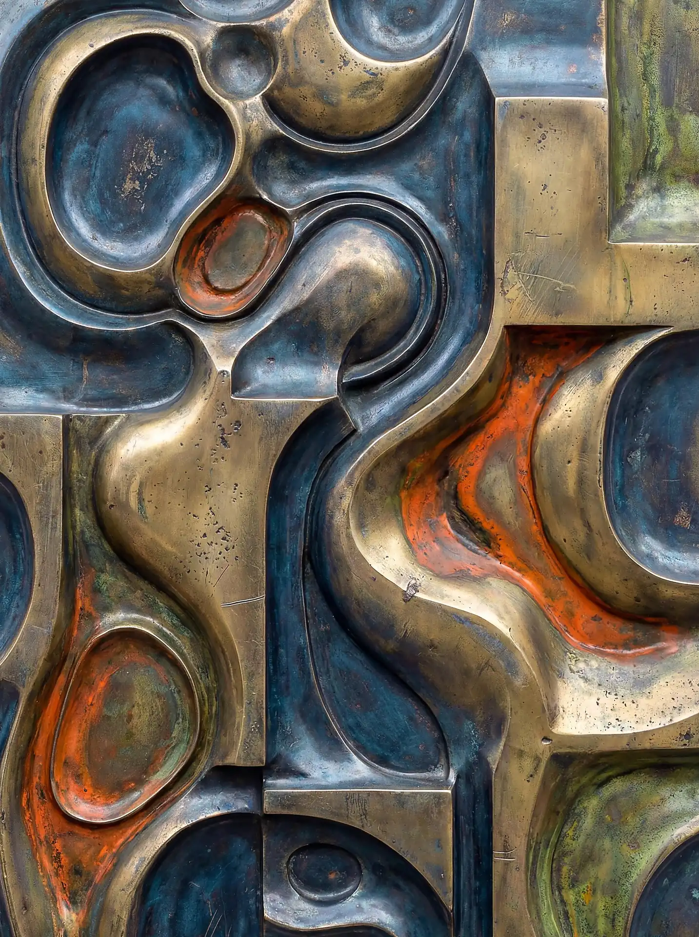 An industrial and modern mood emanates from this cast bronze relief featuring fluid organic shapes and striking orange oxidation. The weathered metallic surface displays deep teal recesses and textured golden highlights that create a sense of tactile depth. Artwork by Constantine Cheshire