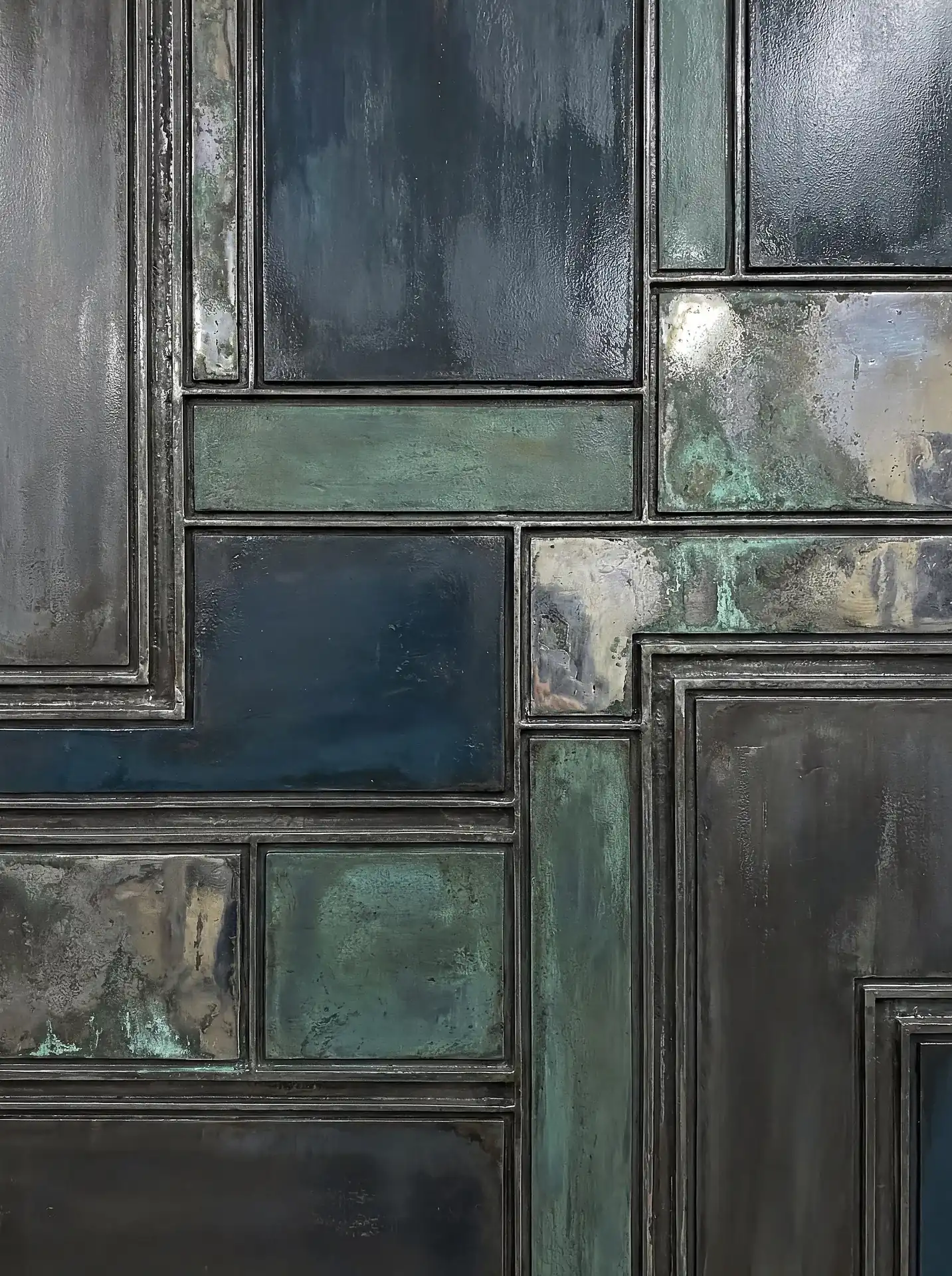 Weathered metallic panels and oxidized copper textures define this striking geometric grid composition. Dark blue and muted teal hues blend with distressed industrial surfaces to create a moody, modern abstract backdrop perfect for architectural and interior design inspiration. Artwork by Constantine Cheshire