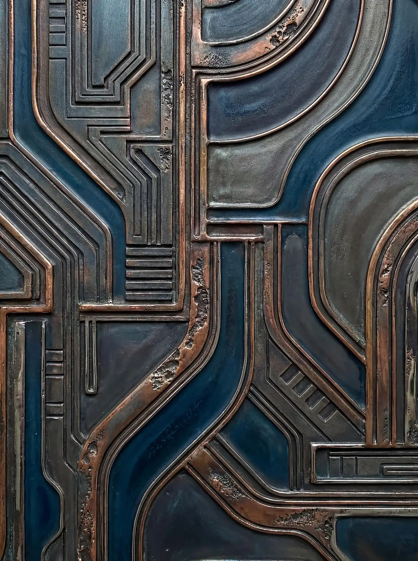 Deep blue shadows and burnished bronze highlights define this intricate geometric relief sculpture. The industrial artwork features weathered metallic textures and interlocking paths that suggest a futuristic circuit board or mechanical blueprint. Artwork by Constantine Cheshire