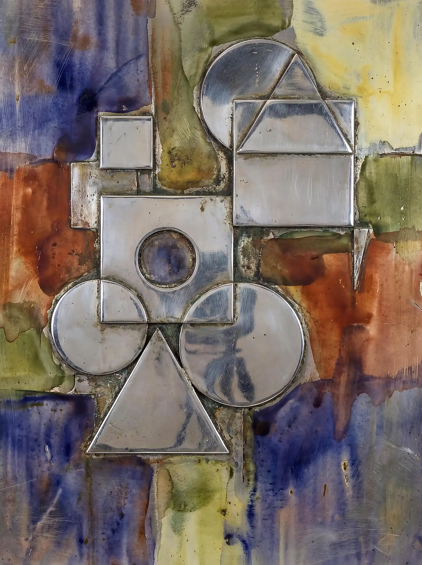 Geometric metal forms of polished steel and chrome create a sophisticated relief sculpture against a weathered multicolored background. This composition features circles, squares, and triangles in a balanced arrangement that blends reflective industrial materials with expressive, distressed textures of indigo and rust. Artwork by Constantine Cheshire