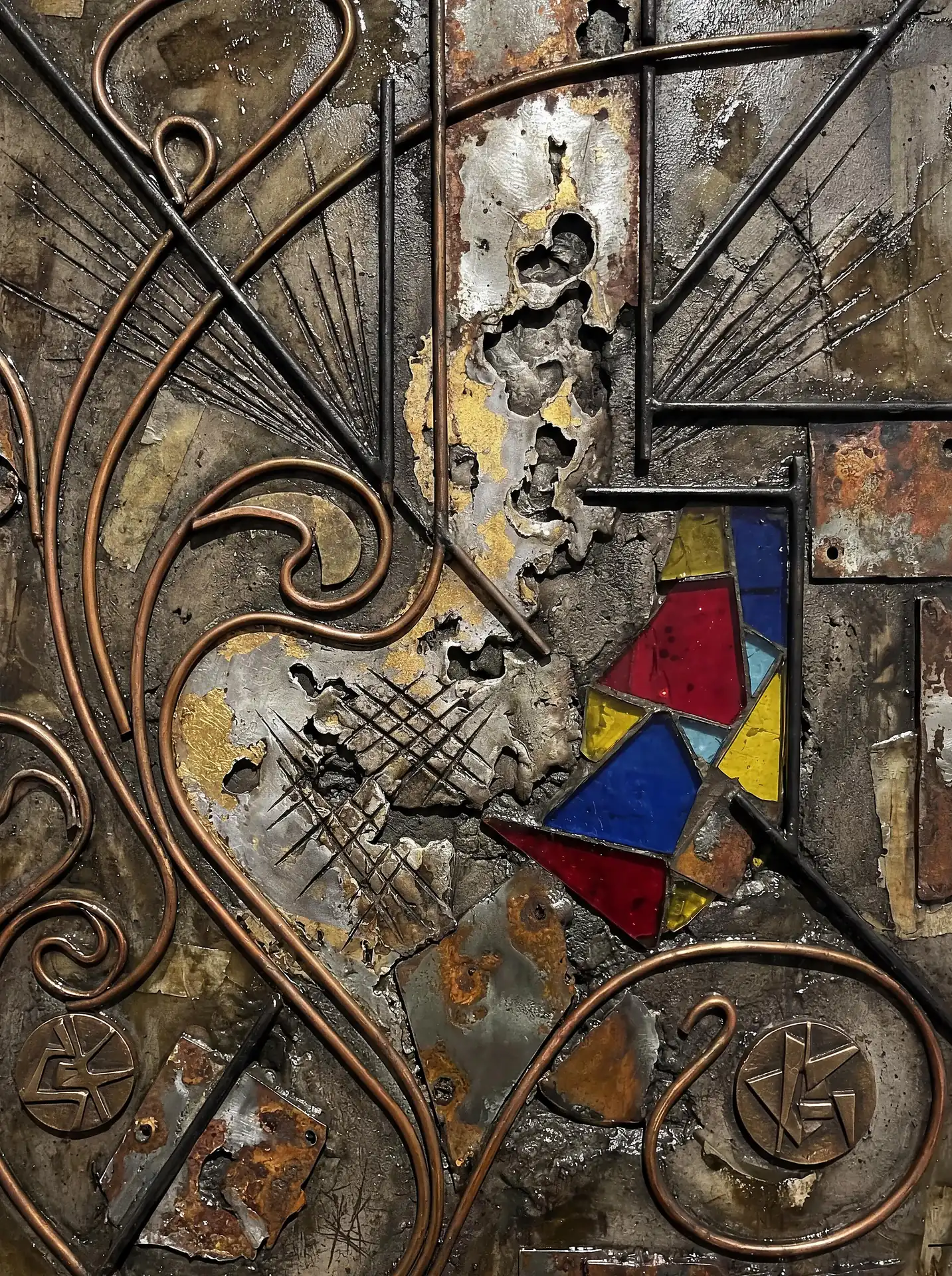 Gritty industrial energy emanates from this complex relief featuring curved copper rods and bright primary-colored glass. This abstract wall sculpture combines rusted metal plates with intricate textures to create a weathered, modern aesthetic. Artwork by Constantine Cheshire