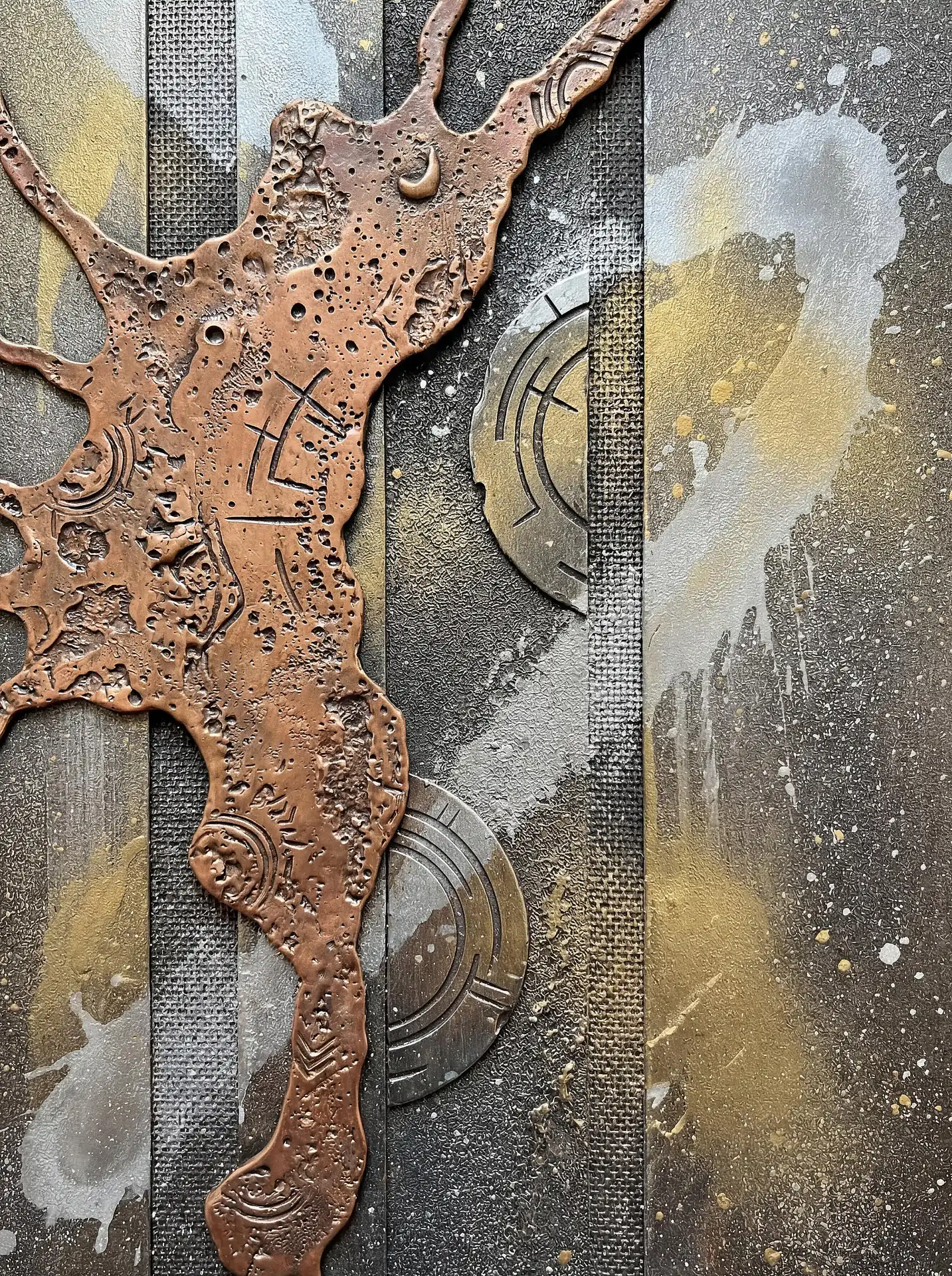 Textured copper shapes and etched metallic circles form a complex mixed-media abstract artwork on canvas. The industrial aesthetic features golden splatters and deep gray tones, creating a moody and tactile sense of ancient technology or alchemy. Artwork by Constantine Cheshire